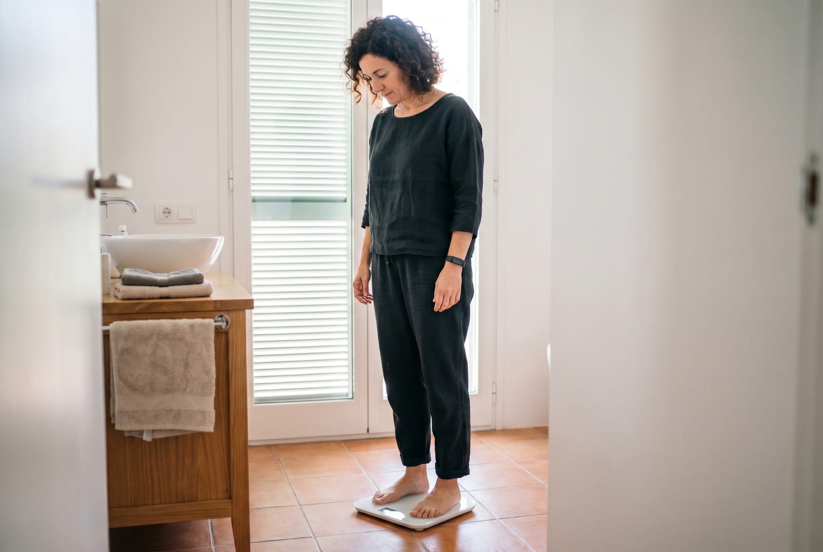 Mujer en un baño con luz tenue bajando de una balanza inteligente, mirando el resultado - Generado por AI