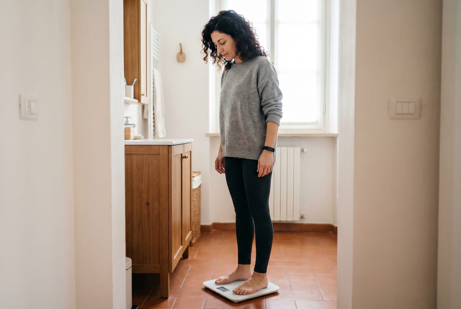 Donna in un bagno dalla luce soffusa che scende da una bilancia smart, dando un'occhiata al display - Generata da AI